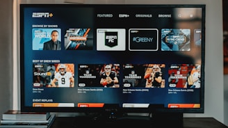 A television screen displaying the ESPN+ streaming interface with various sports-related shows and categories. The screen includes sections such as 'Browse by Shows' and 'Best of Drew Brees' with thumbnails of sports programs featuring athletes in action and analysts.